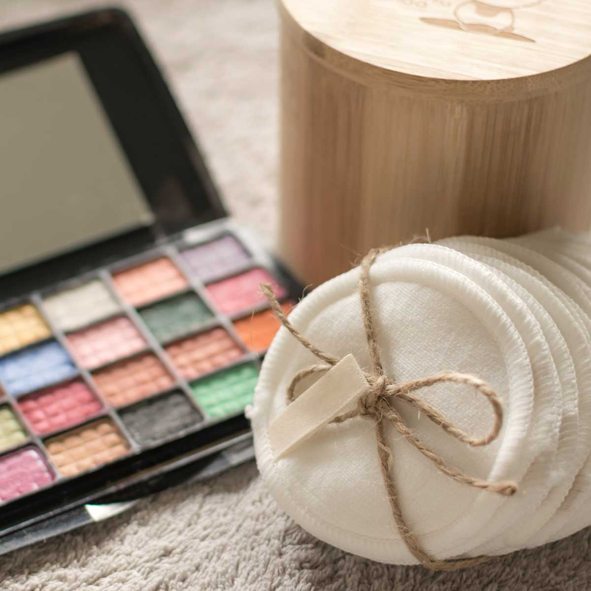 Ein Stapel waschbarer, gekaufter Baumwoll-Pads zum Abschminken mit einer Lidschatten-Palette im Hintergrund